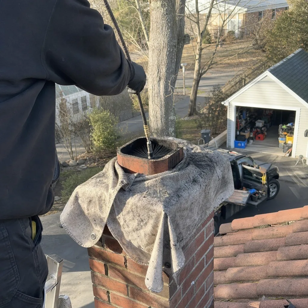 Professional chimney sweep cleaning a brick chimney flue from the roof
